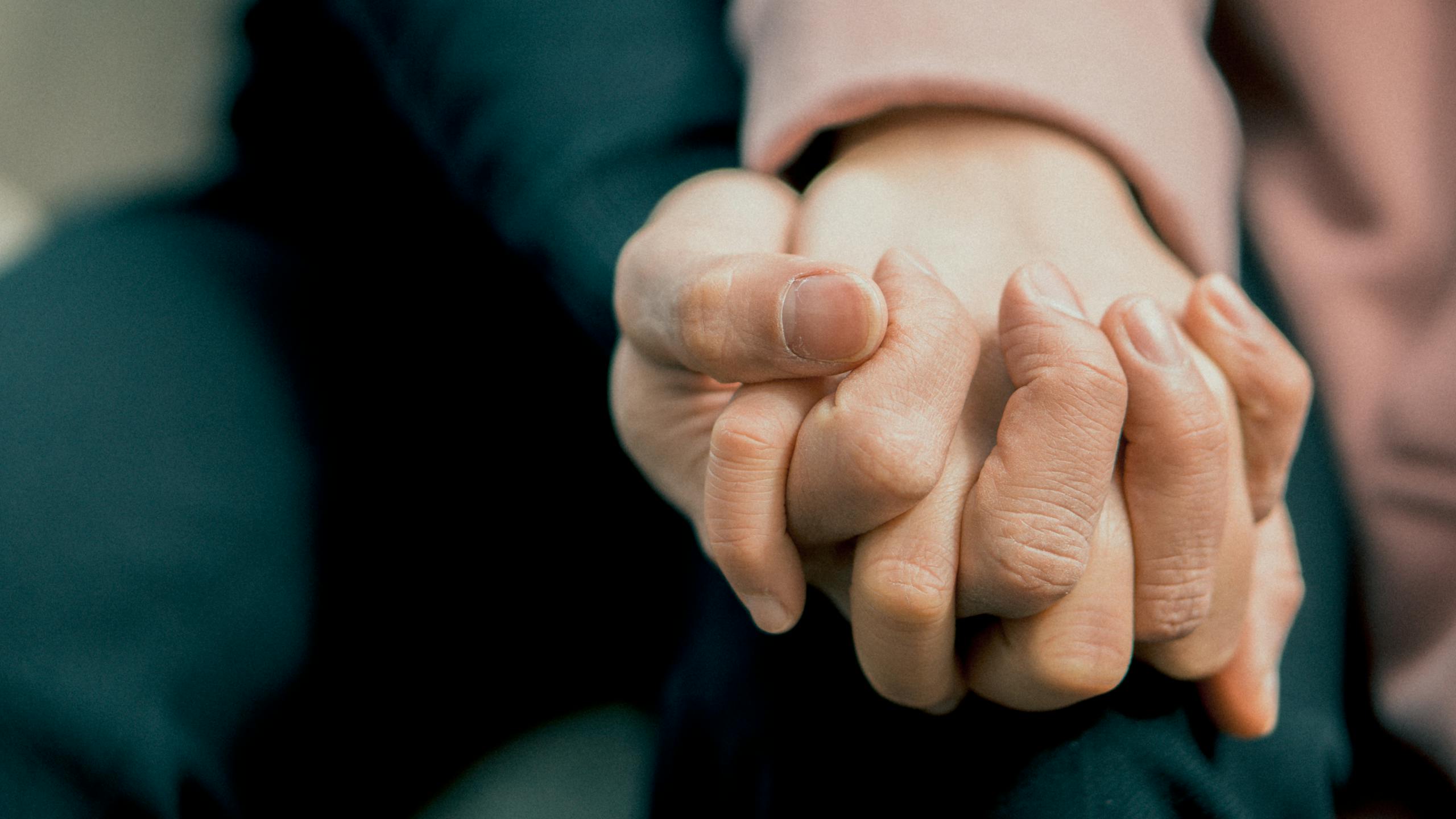 A close-up photo capturing two adult hands holding each other, symbolizing love and support.
