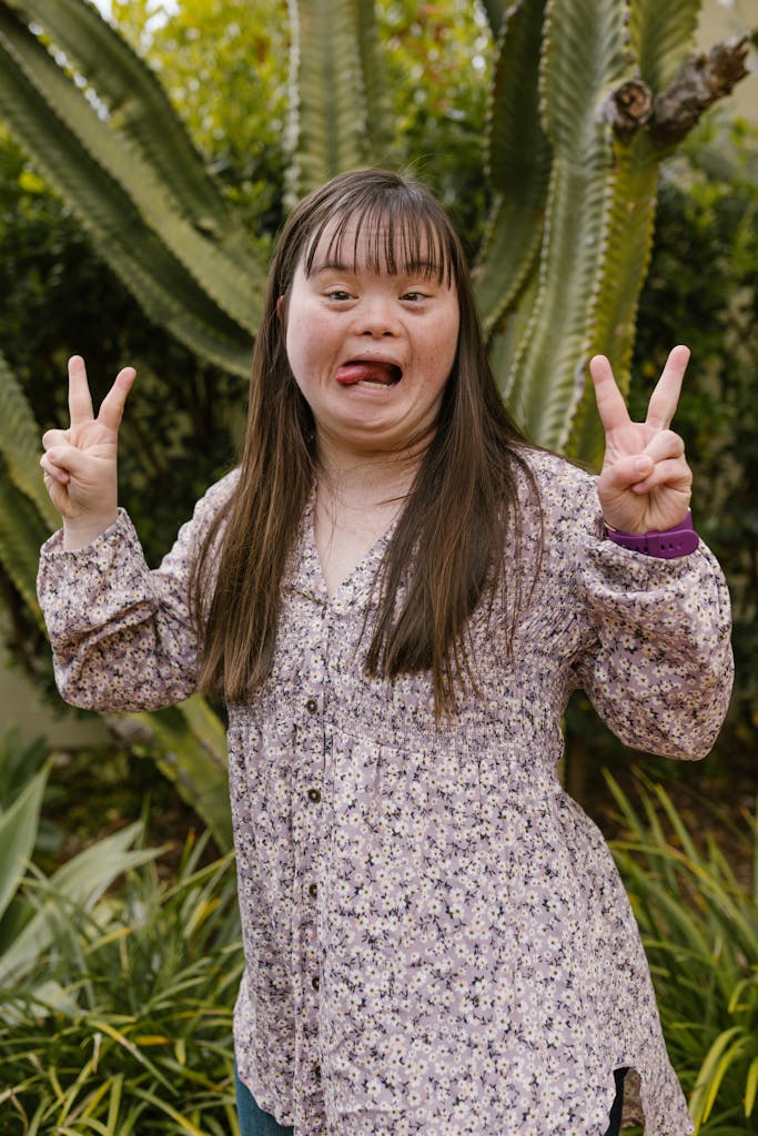 Playful young woman with Down syndrome posing with peace signs in a garden.